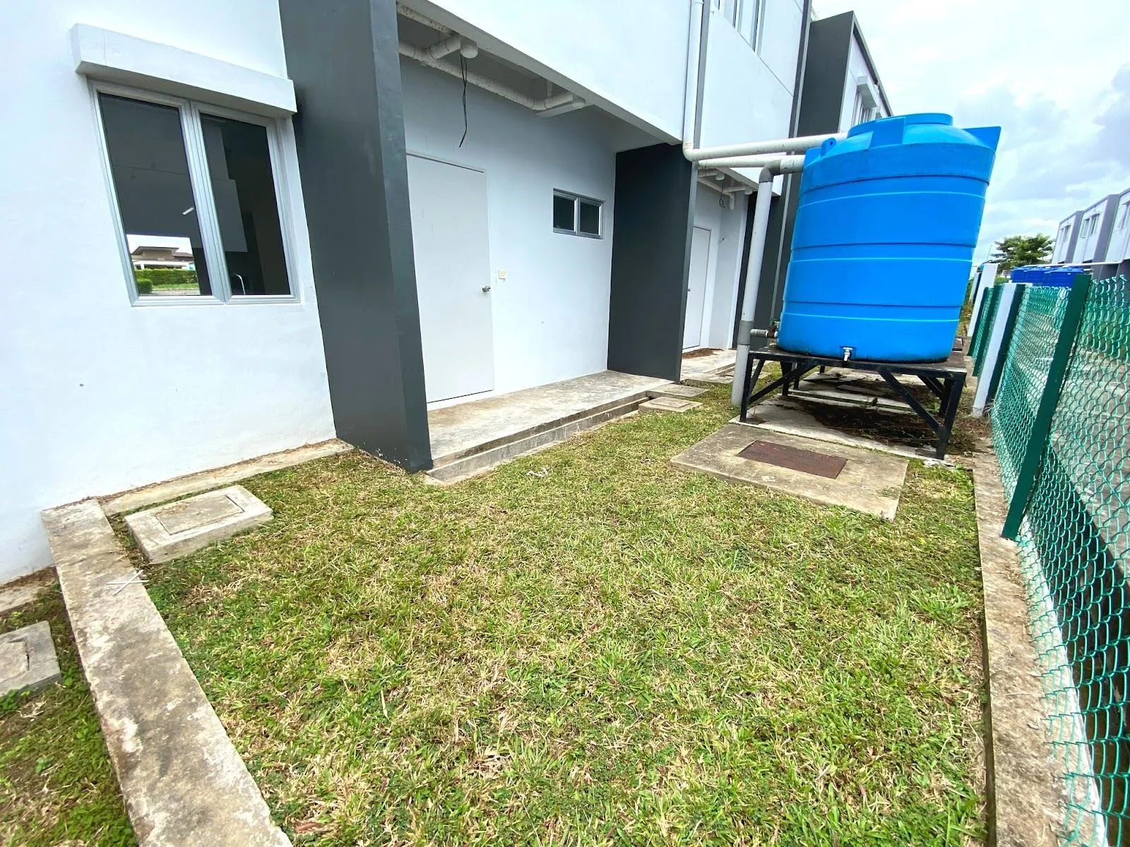 Type C3 backyard with turf, a water tank and chain-link fence — photograph from the developer’s presentation at Bandar Sri Indah, Jalan Apas, Tawau, Sabah