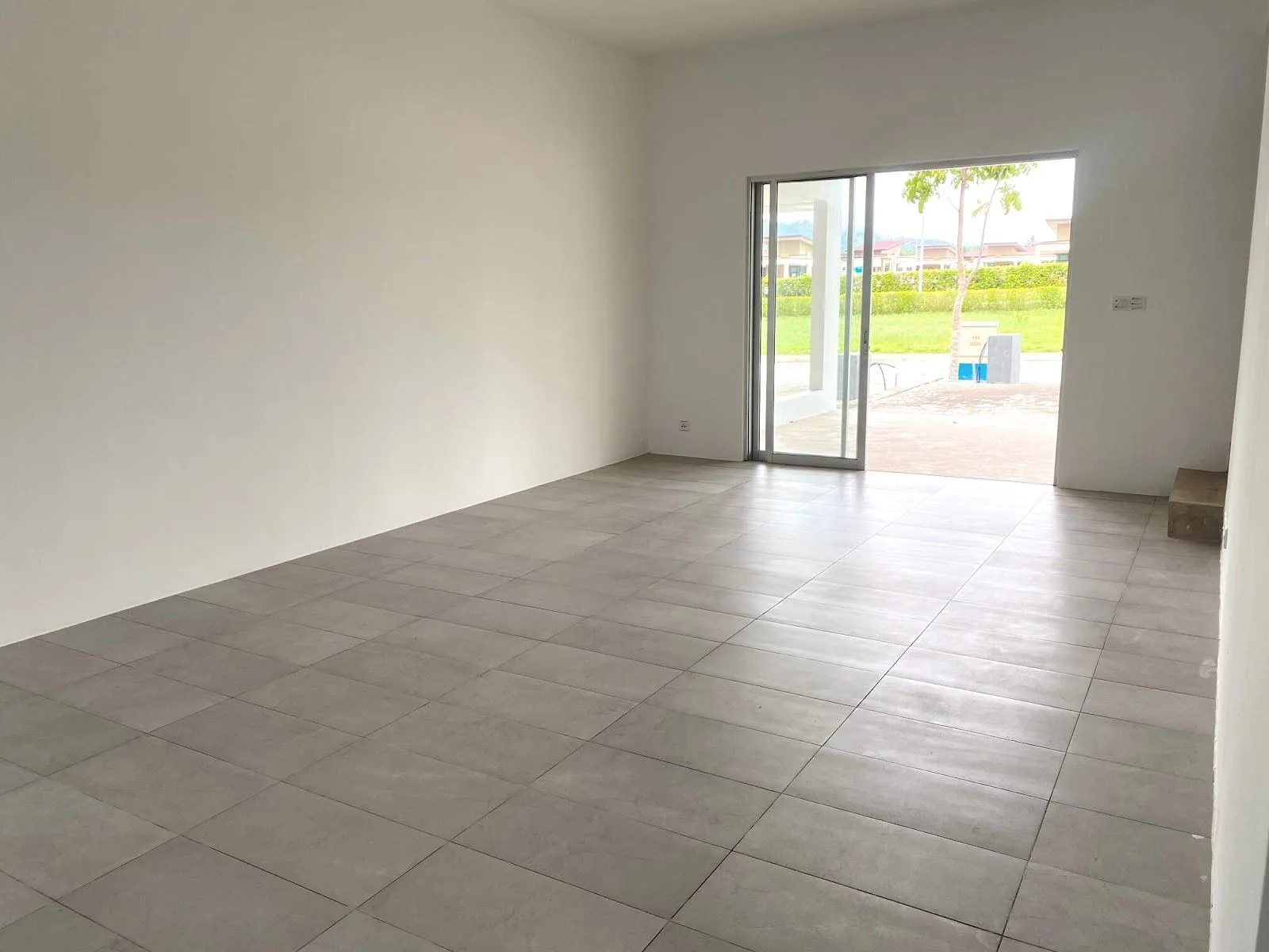 Type C3 living room as handed over, unfurnished, with tiled floor and sliding door to the car porch — photograph from the developer’s presentation at Bandar Sri Indah, Jalan Apas, Tawau, Sabah